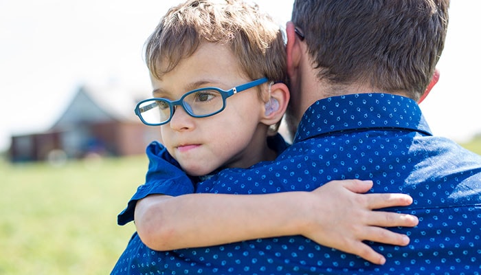 A boy with a hearing aid, hugging his father.