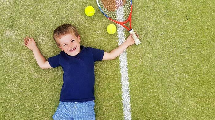 The boy lies on the tennis court and smiles
